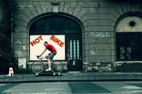 Racing cyclist travelling on free motion cycling rollers in front of a rundown house with an empty shop