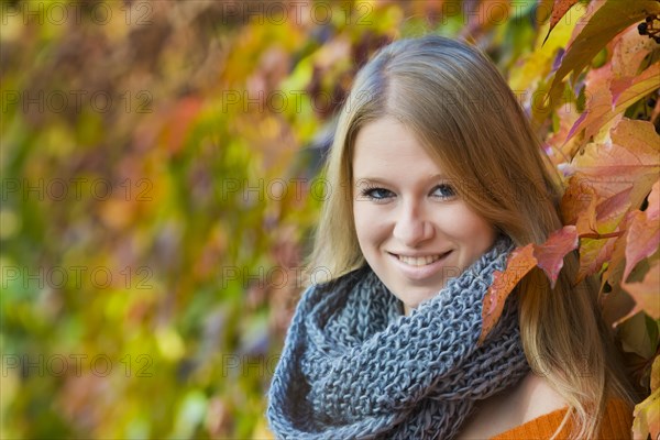 Young woman wearing a thick scarf in front of colourful autumn leaves