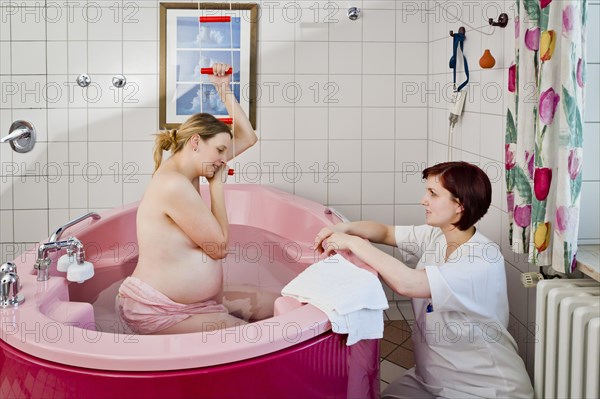 Woman during childbirth in a birthing bath in the maternity delivery room beside her midwife