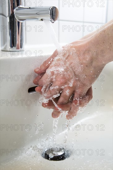 Person washing their hands under running water from a faucet