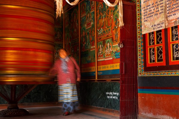 A female devotee spinning a large prayer wheel