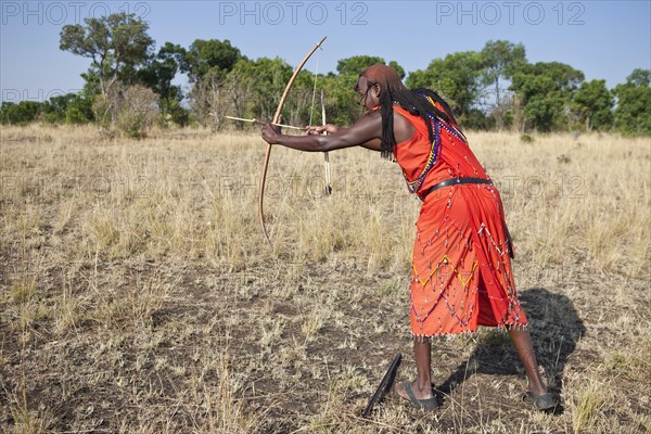Maasai warrior wearing traditional dress while doing archery with a bow and arrow