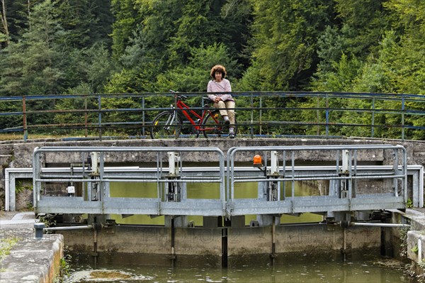 Spectator with a bicycle observing a houseboat passing through a lock on the Canal des Vosges
