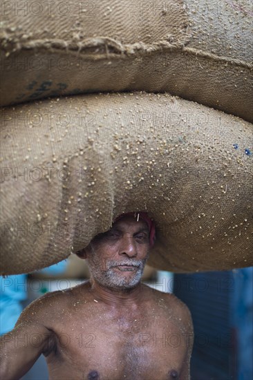 Elderly man carrying two bags filled with spices on his head