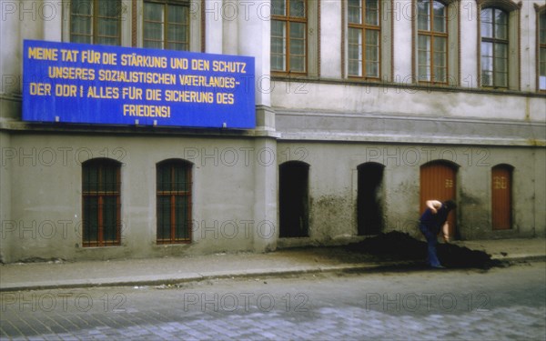 Worker shovelling coal from the street into a coal cellar next to a socialist propaganda sign