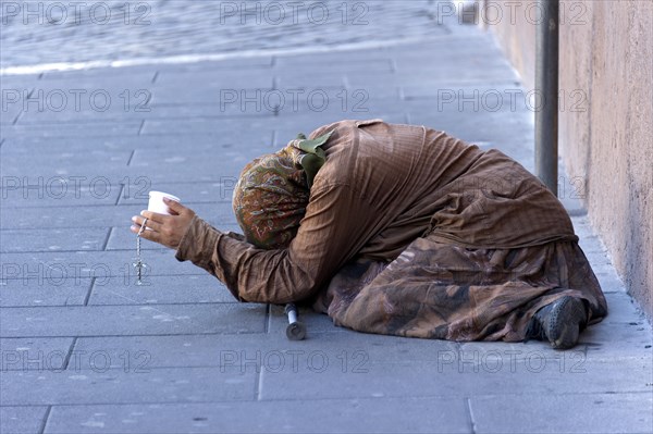 Female beggar holding a plastic cup in a street of the old town