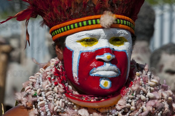 Member of a tribe in a colourfully decorated costume with face paint at the traditional sing-sing gathering