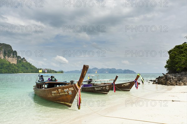 Three longtail boats on a white sandy beach