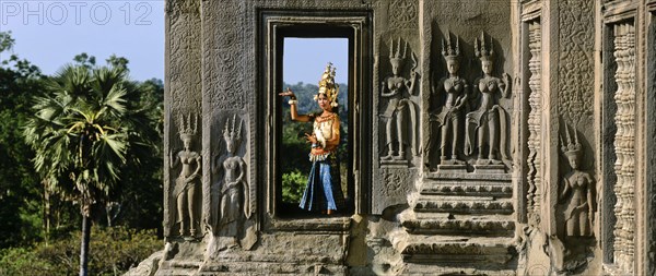 Temple dancer or apsara in a window of the temple of Angkor Wat beside apsara reliefs