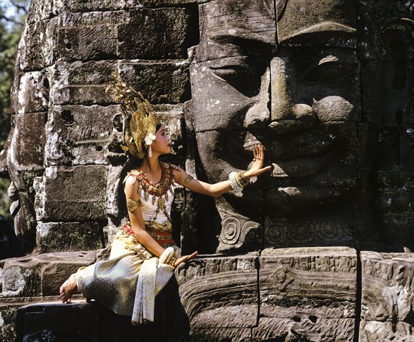 Temple dancer or apsara sitting in front of a face tower at Bayon Temple