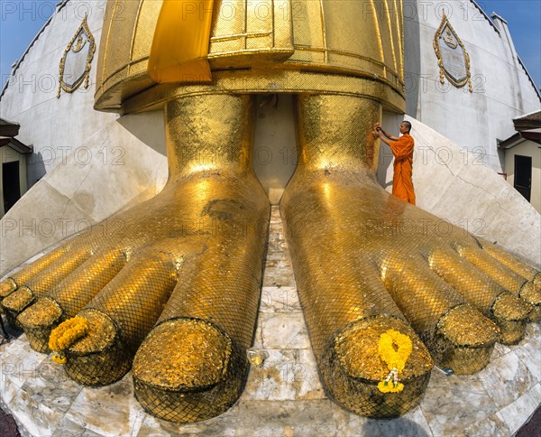Monk praying at the feet of the golden Buddha statue of Wat Intharawihan