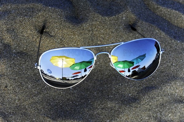 Parasols are reflected in sunglasses lying in the sand