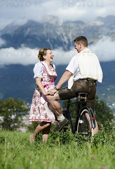 Man and a woman wearing traditional costume with an old bicycle within a natural landscape