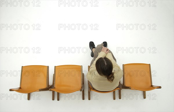 Woman wearing conservative clothes sitting on one of a row of four orange chairs