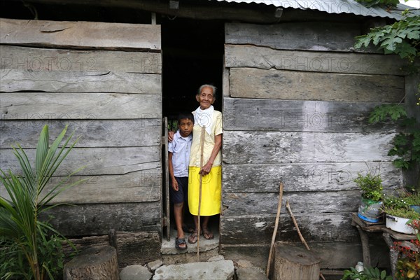 Girl and elderly woman standing at the entrance of her hut in a poor village