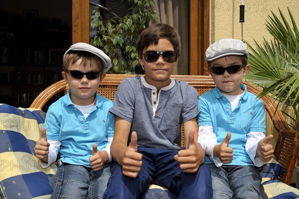 Twins and their older brother sitting together on a bench on a terrace
