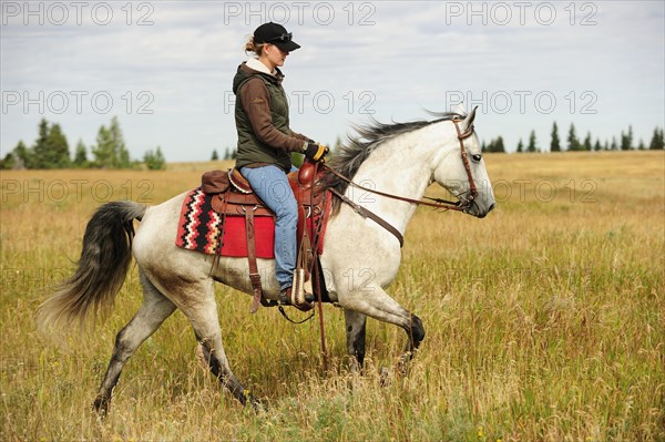 Woman riding on a gray horse across the prairie