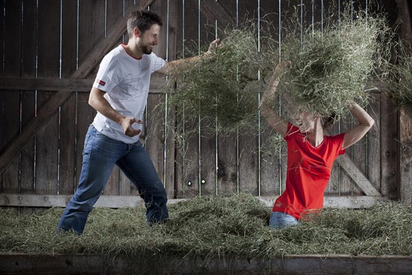 Young couple throwing hay at each other on a farm