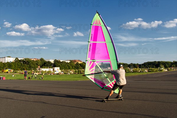 Windskater practicing on the asphalt runway with a windsurfer sail and a longboard