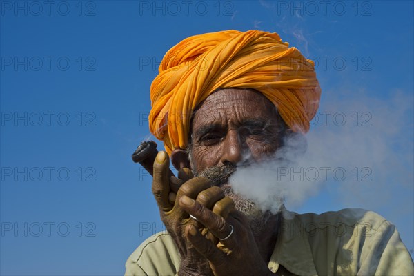 Elderly Rajasthani man with an orange turban smoking a hash pipe or hooka