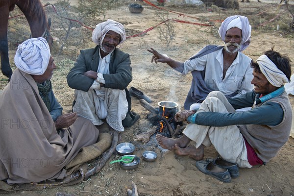 Four Indian men in turbans sitting on the ground having a conversation