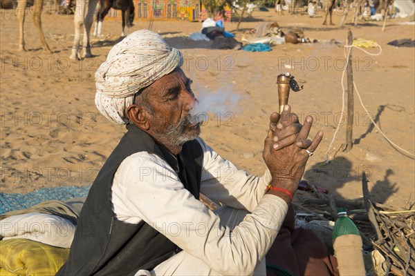 Indian with a turban sitting on the ground smoking a hash pipe