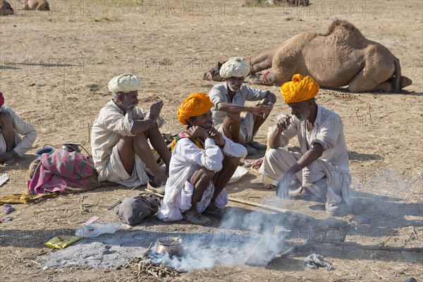 Four elderly Indian men with turbans and wearing the traditional Dhoti garment squatting on the ground