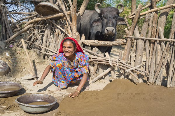 Friendly young woman in traditional dress plastering the floor of a courtyard with a mixture of water