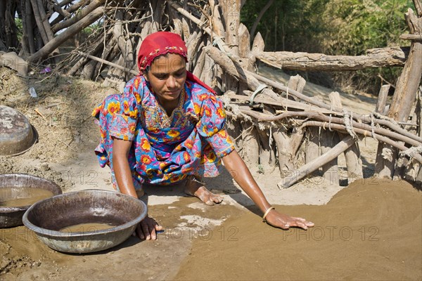 Friendly young woman in traditional dress plastering the floor of a courtyard with a mixture of water