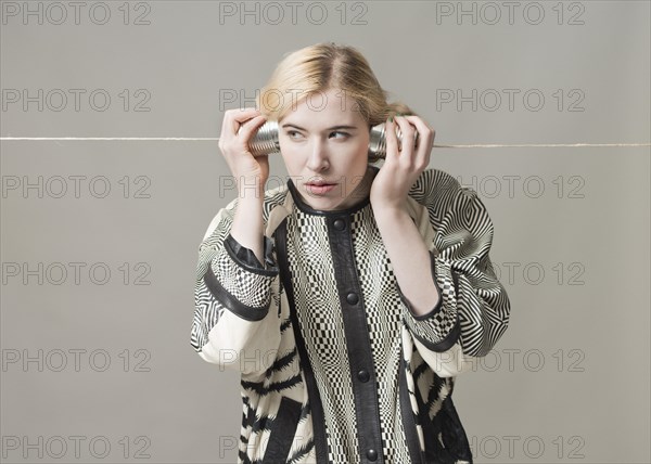 Blond woman listening with tin can phone