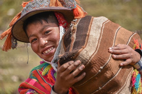 Indio boy with hat with colorful ribbons and poncho wearing sack with potatoes