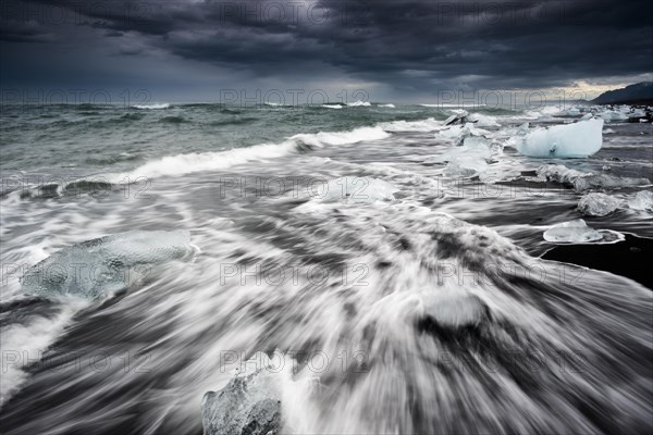 Pieces of ice on black beach lapped by the sea