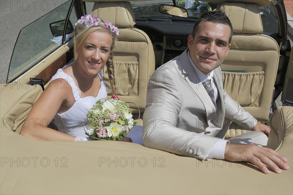 Bride and groom posing in the back seat of an open car