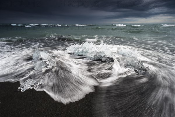 Pieces of ice on the black beach lapped by the sea