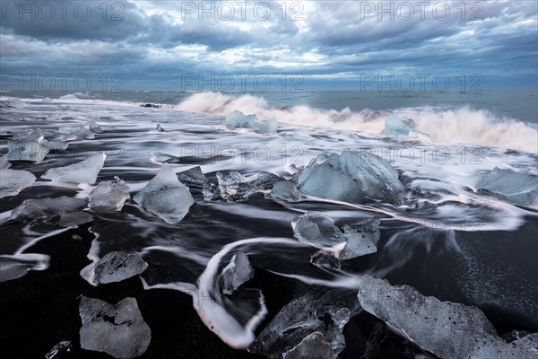 Pieces of ice on black beach lapped by the sea