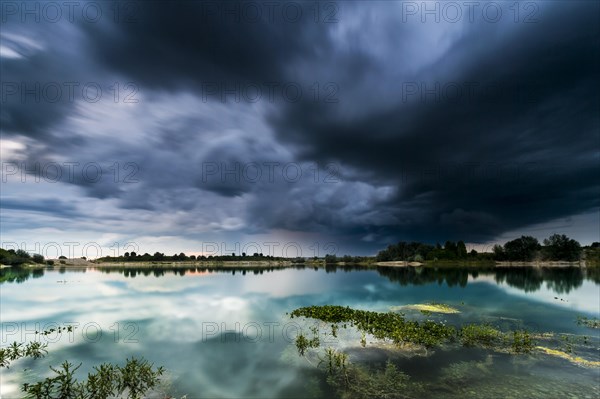 Storm clouds over a quarry lake with water plants