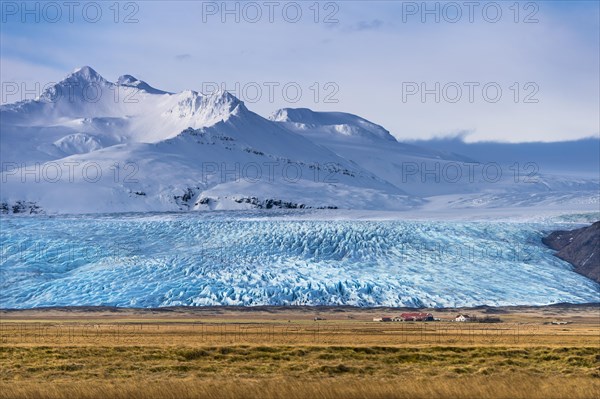 Icelandic farmstead with glacier tongue and snow-covered mountains