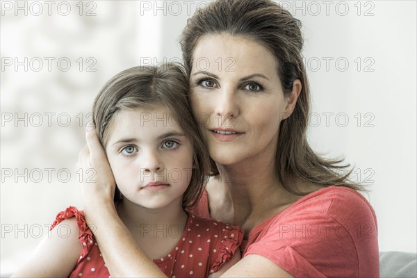 Mother and daughter sit together on the couch and look into the camera