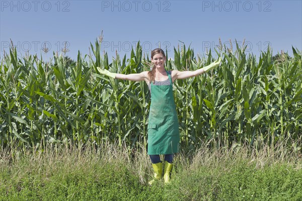 Young woman in work clothes standing with outstretched arms in front of a maize field