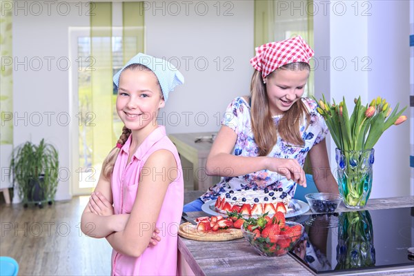 Teenage girls baking a cake at home with fresh fruit