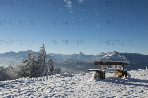 Snow-covered bench in front of Alpine panorama