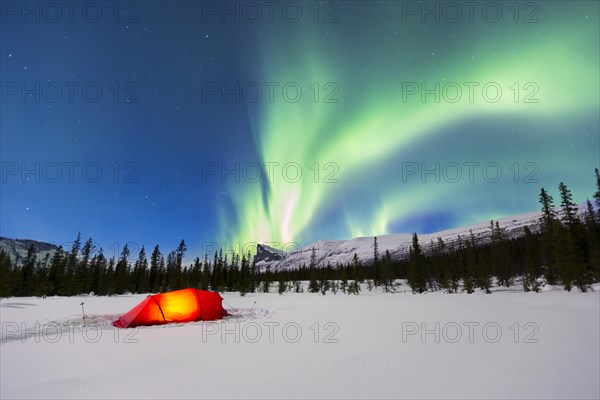 Northern Lights (Aurora borealis) above a red illuminated tent in winter