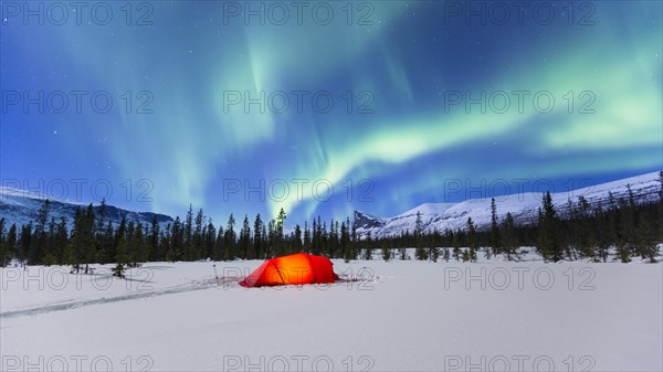 Northern Lights (Aurora borealis) above a red illuminated tent in winter