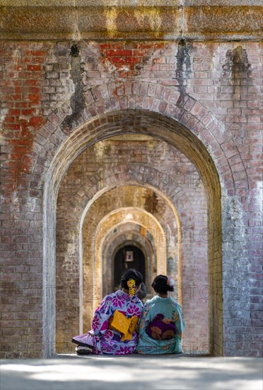 Two Japanese women in kimono sitting at the Suirokaku aqueduct