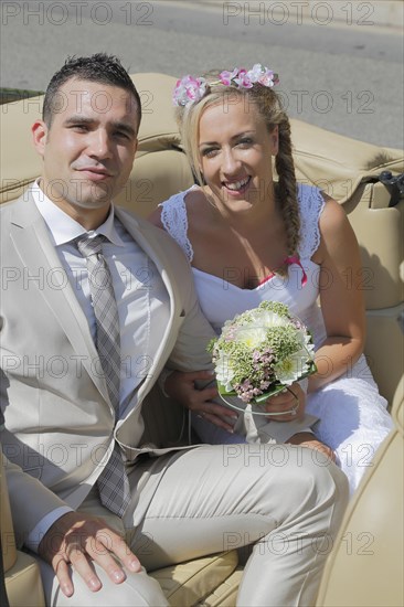 Bride and groom posing in the back seat of an open car