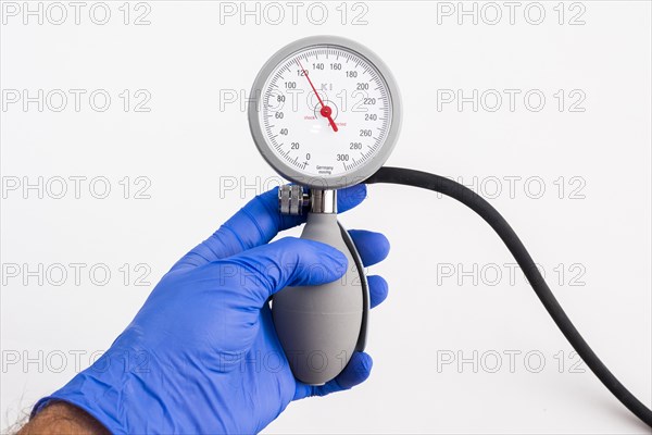 A hand with a blue medical glove is holding a sphygmomanometer