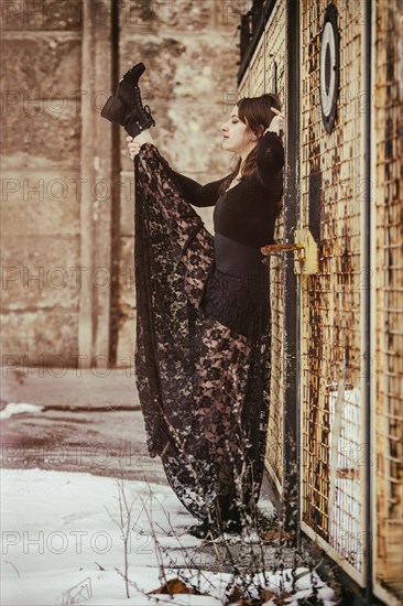 Dancer in a black dress performing in front of an old fence in winter