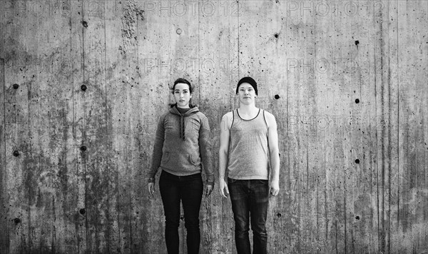 Young woman and man standing in front of concrete wall