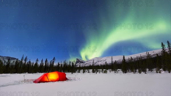 Northern Lights (Aurora borealis) above a red illuminated tent in winter