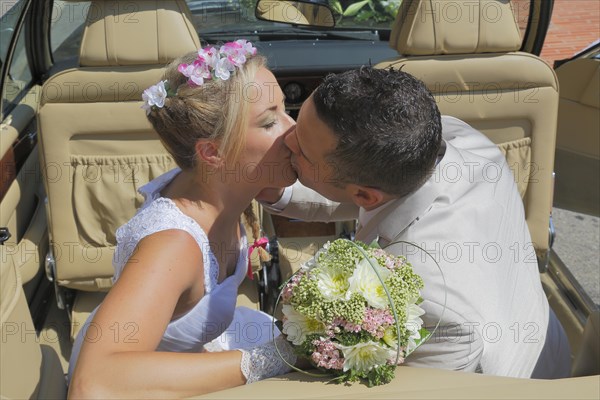 Bride and groom kissing in the back seat of an open car